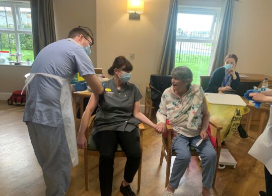Ebor-Court-Care-Assistant-Marie-and-resident-Ann-hold-hands-as-they-receive-the-Covid-19-vaccination-together